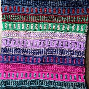 May include: A colourful knitted throw blanket with stripes of various colours, including black, blue, red, green, purple and pink.
