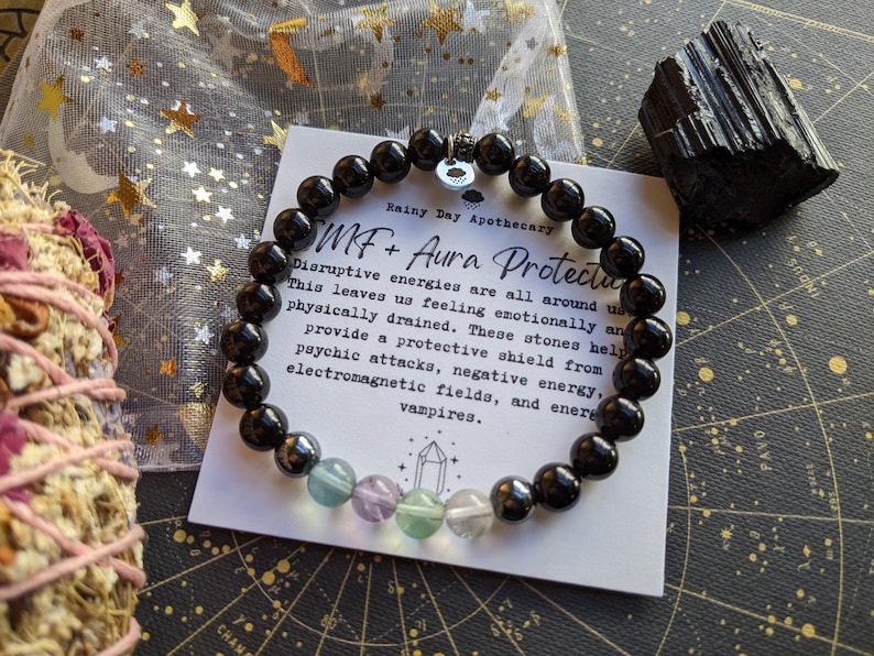 May include: Black onyx beaded bracelet with a charm and a card that reads "MF + Aura Protection". The card explains that the bracelet helps protect against disruptive energies, psychic attacks, negative energy, electromagnetic fields, and energy vampires.