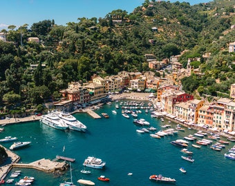 May include: An aerial view of a colorful Italian village with a harbor filled with boats. The village is built on a hillside and has many buildings with terracotta roofs. The harbor is filled with boats of all sizes, including a large yacht.