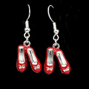 May include: A pair of red and silver dangle earrings shaped like ruby slippers. The earrings have a silver bow detail and a silver hook.