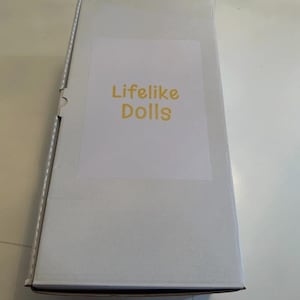 May include: A white cardboard box with the text "Lifelike Dolls" in yellow letters on a white label. The box is rectangular and appears to be sealed.