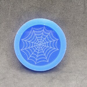 May include: A blue silicone mold with a white spiderweb design. The mold is round and has a smooth surface.