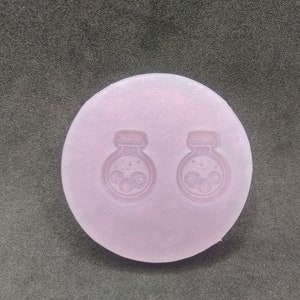May include: A light purple silicone mold with two impressions of a small potion bottle with a cork and swirling designs inside.