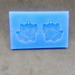 May include: A blue silicone mold with two axolotl designs. Each axolotl is wearing glasses and holding a heart.