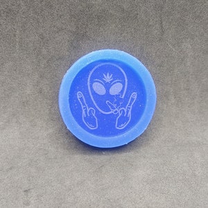May include: A blue round silicone mold with a white alien design. The alien is smoking a joint and giving the peace sign with both hands.