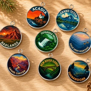 May include: Eight circular silver-toned metal charms featuring colorful landscape illustrations of U.S. National Parks. Each charm displays a specific park name including Acadia, Grand Teton, Badlands, Cuyahoga Valley, Great Smoky Mountains, Grand Canyon, New River Gorge, and Shenandoah.