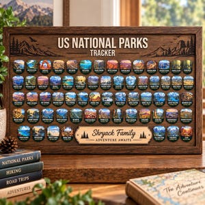 Puede incluir: Un tablero de madera para rastrear los Parques Nacionales de EE. UU. con filas de pequeños emblemas coloridos. El texto superior dice US NATIONAL PARKS TRACKER. Una placa central muestra el texto Shryack Family ADVENTURE AWAITS con iconos de árboles.