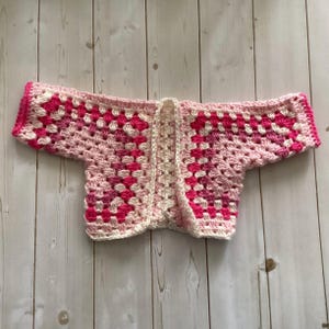 A crocheted cardigan with a black, brown, white, and blue color pattern. The cardigan is open in the front and has a loose fit.