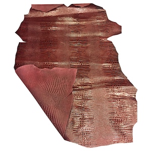 May include: A sheet of reddish-brown leather with a textured, crocodile-like pattern. The underside of the leather is a lighter shade of red. The leather is folded over, revealing the contrasting interior.