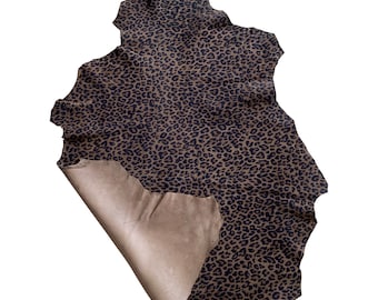 May include: A brown leather hide with a black leopard print pattern. The hide is folded in half, revealing the unprinted side.