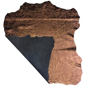 May include: A piece of brown leather with a metallic gold pattern. The leather is folded over, revealing a dark blue underside. The edges of the leather are uneven, giving it a natural, organic look.
