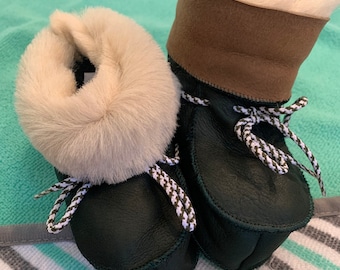 May include: A pair of dark green leather baby booties with white and black laces. The booties have a white fur lining and a brown leather cuff.