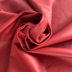 May include: Close-up of a deep red leather fabric, folded and draped in soft, flowing folds.