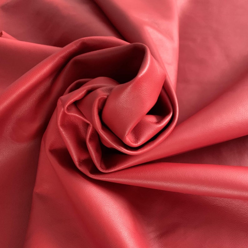 May include: Close-up of a deep red leather fabric, folded and draped in soft, flowing folds.