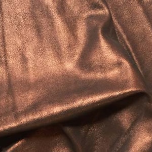 May include: Close-up of a bronze-colored fabric with a metallic sheen. The material is heavily textured, with folds and shadows creating depth. The fabric appears soft and pliable, with a subtle sparkle.