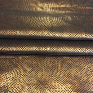 May include: Close-up of a gold snakeskin fabric with a textured pattern. The fabric is folded in three layers, showing the texture from different angles.