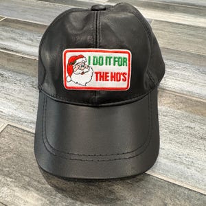 May include: Black leather baseball cap with a red, white, and green embroidered patch that says "I do it for the ho's" and features a cartoon image of Santa Claus.