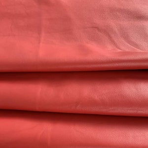 May include: Close-up of a folded piece of red leather. The leather has a smooth, slightly textured surface.