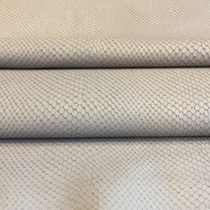 May include: Close-up of a folded piece of light gray faux leather fabric. The material has a textured, scale-like pattern, creating a reptile skin appearance. The fabric is folded in horizontal layers, showing the texture and color variations.