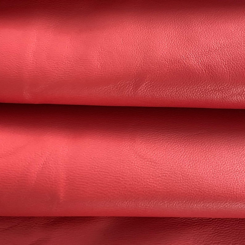 May include: Close-up of a folded piece of red leather. The leather has a textured surface and a slightly grainy appearance.
