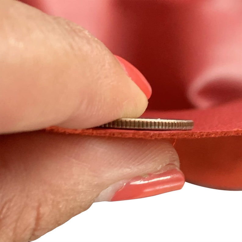 May include: Close-up of a red fabric being held by a hand. A coin is used to show the thickness of the fabric.