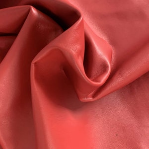 May include: Close-up of a red leather fabric with a smooth, textured surface. The leather is folded and draped, showing its flexibility and softness.