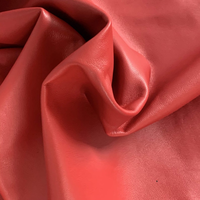 May include: Close-up of a red leather fabric with a smooth, textured surface. The leather is folded and draped, showing its flexibility and softness.