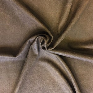 May include: A close-up of a swatch of brown fabric with a textured, dotted pattern. The fabric is folded and swirled, creating shadows and highlights. The material appears soft and pliable, suitable for upholstery or apparel.