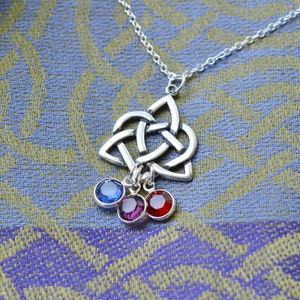 Puede incluir: Un collar con un colgante de nudo celta plateado y tres abalorios colgantes. Los abalorios son piedras preciosas azules, moradas y rojas.