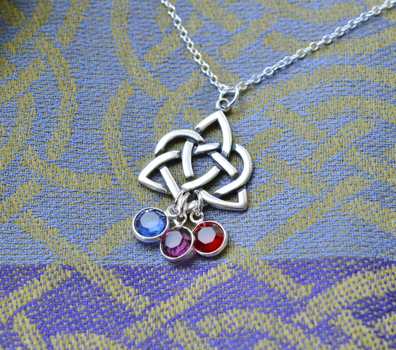 Puede incluir: Un collar con un colgante de nudo celta plateado y tres abalorios colgantes. Los abalorios son piedras preciosas azules, moradas y rojas.