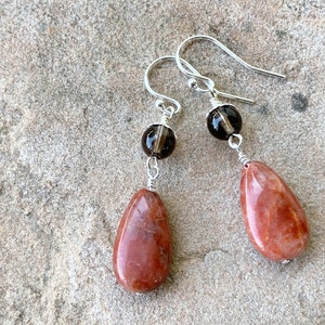 May include: A pair of dangle earrings with red jasper teardrop shaped stones and smoky quartz beads.
