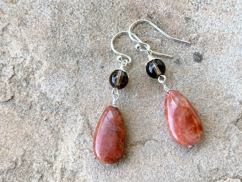 May include: A pair of dangle earrings with red jasper teardrop shaped stones and smoky quartz beads.