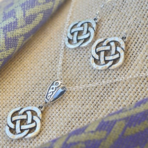 May include: A silver Celtic knot necklace and earrings set. The necklace features a pendant with a detailed knot design and a small charm with a Celtic knot. The earrings are also detailed with a Celtic knot design.