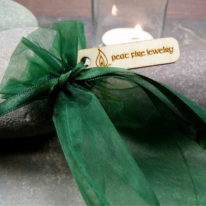 May include: A green organza gift bag with a wooden tag that reads "peat fire jewelry".