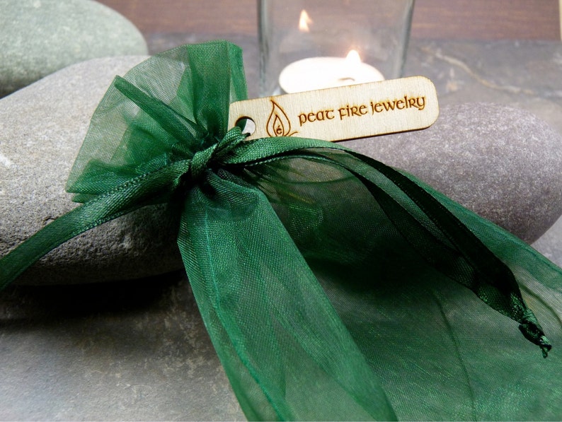 May include: A green organza gift bag with a wooden tag that reads "peat fire jewelry".