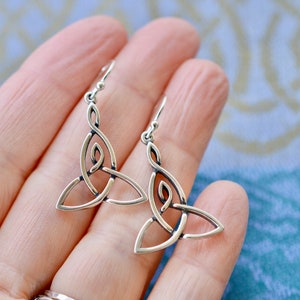 May include: Silver Celtic knot earrings with a triangular design. The earrings are dangle style and have a hook closure.
