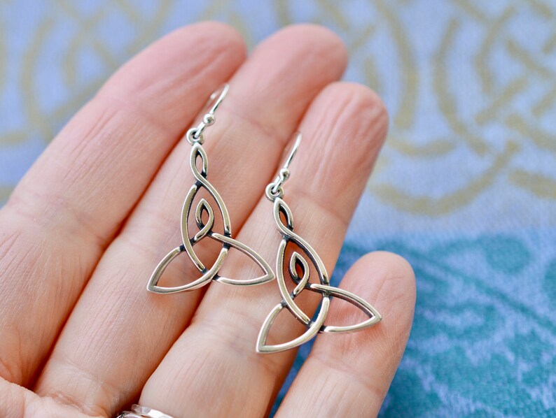 May include: Silver Celtic knot earrings with a triangular design. The earrings are dangle style and have a hook closure.