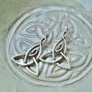 May include: A pair of silver Celtic knot earrings with a delicate design. The earrings are hanging from a silver hook.