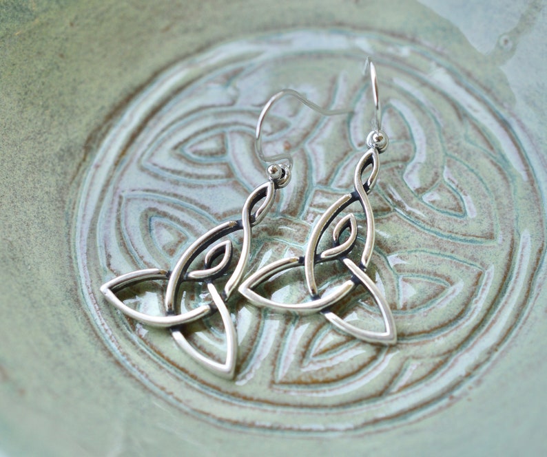 May include: A pair of silver Celtic knot earrings with a delicate design. The earrings are hanging from a silver hook.
