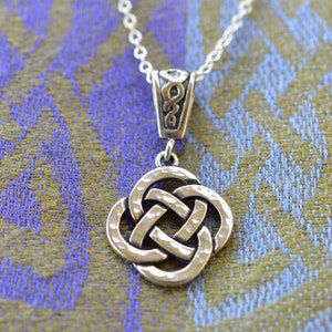 May include: Silver Celtic knot pendant necklace with a detailed, textured design. The pendant is shaped like a square with four interlocked knots.