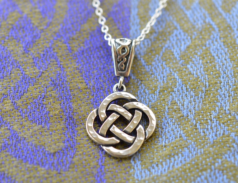 May include: Silver Celtic knot pendant necklace with a detailed, textured design. The pendant is shaped like a square with four interlocked knots.