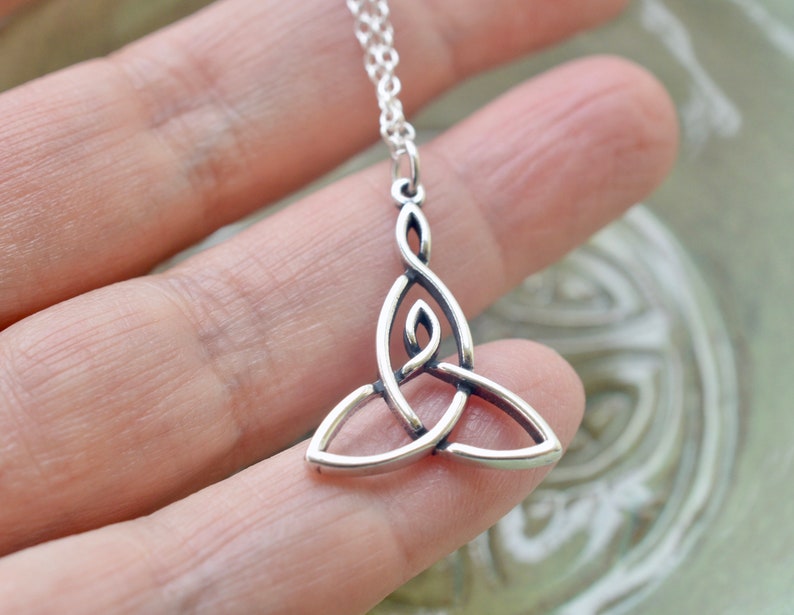 May include: A silver Celtic knot pendant necklace. The pendant is a traditional triquetra design, which symbolizes the trinity. The necklace is on a silver chain.