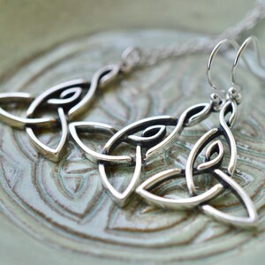 May include: Silver Celtic knot earrings with a dangling design. The earrings are made of a silver metal and have a traditional Celtic knot pattern.