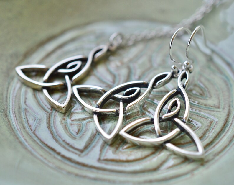 May include: Silver Celtic knot earrings with a dangling design. The earrings are made of a silver metal and have a traditional Celtic knot pattern.