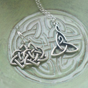 May include: A pair of silver Celtic knot earrings and a silver Celtic knot pendant necklace on a green background.