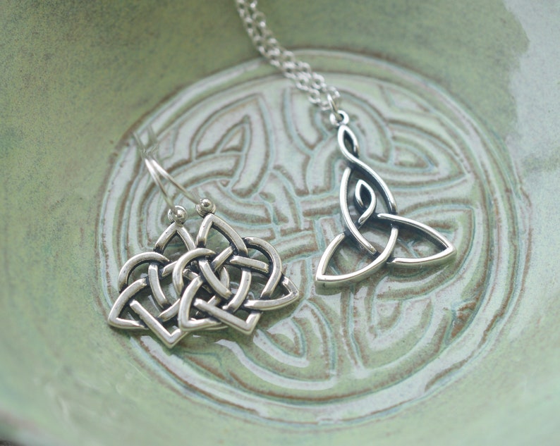 May include: A pair of silver Celtic knot earrings and a silver Celtic knot pendant necklace on a green background.
