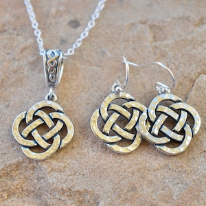May include: A silver Celtic knot necklace and matching earrings. The necklace has a delicate chain and a pendant with a hammered finish. The earrings are also hammered and have a hook closure.