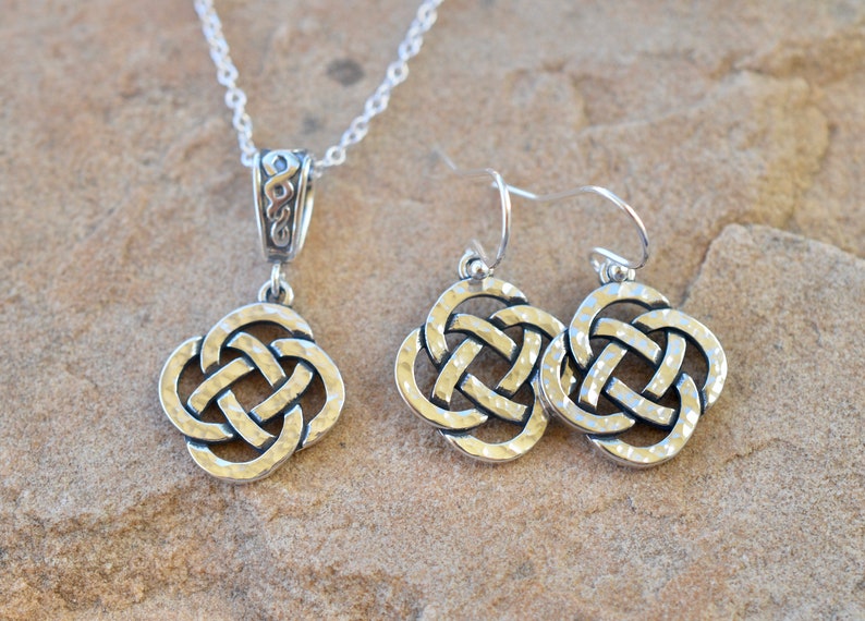May include: A silver Celtic knot necklace and matching earrings. The necklace has a delicate chain and a pendant with a hammered finish. The earrings are also hammered and have a hook closure.