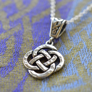 May include: Silver Celtic knot pendant necklace with a hammered texture. The pendant is in the shape of a square knot with four loops. The necklace is on a silver chain.