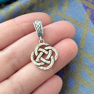 May include: A silver Celtic knot pendant with a textured finish. The pendant is in the shape of a four-leaf clover and has a loop at the top for attaching to a chain.